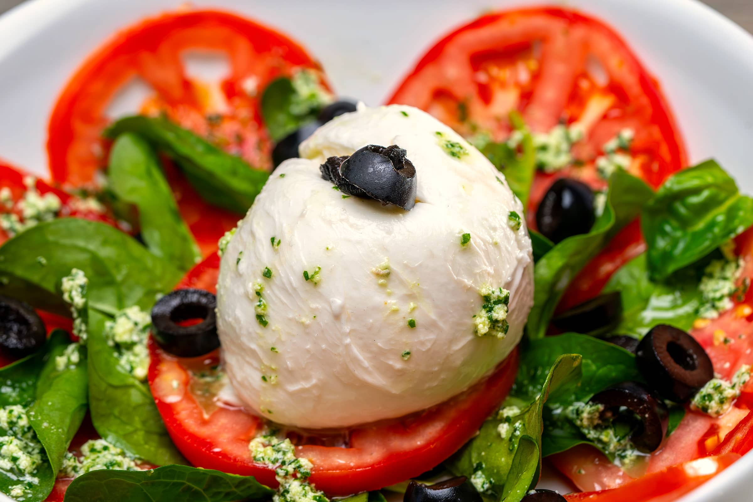 Burrata auf Tomaten mit Spinat, Oliven und Pesto